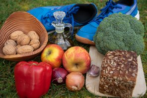 Frisches Obst, Gemüse und ein Brot liegen neben einem Paar Joggingschuhe auf der Wiese.