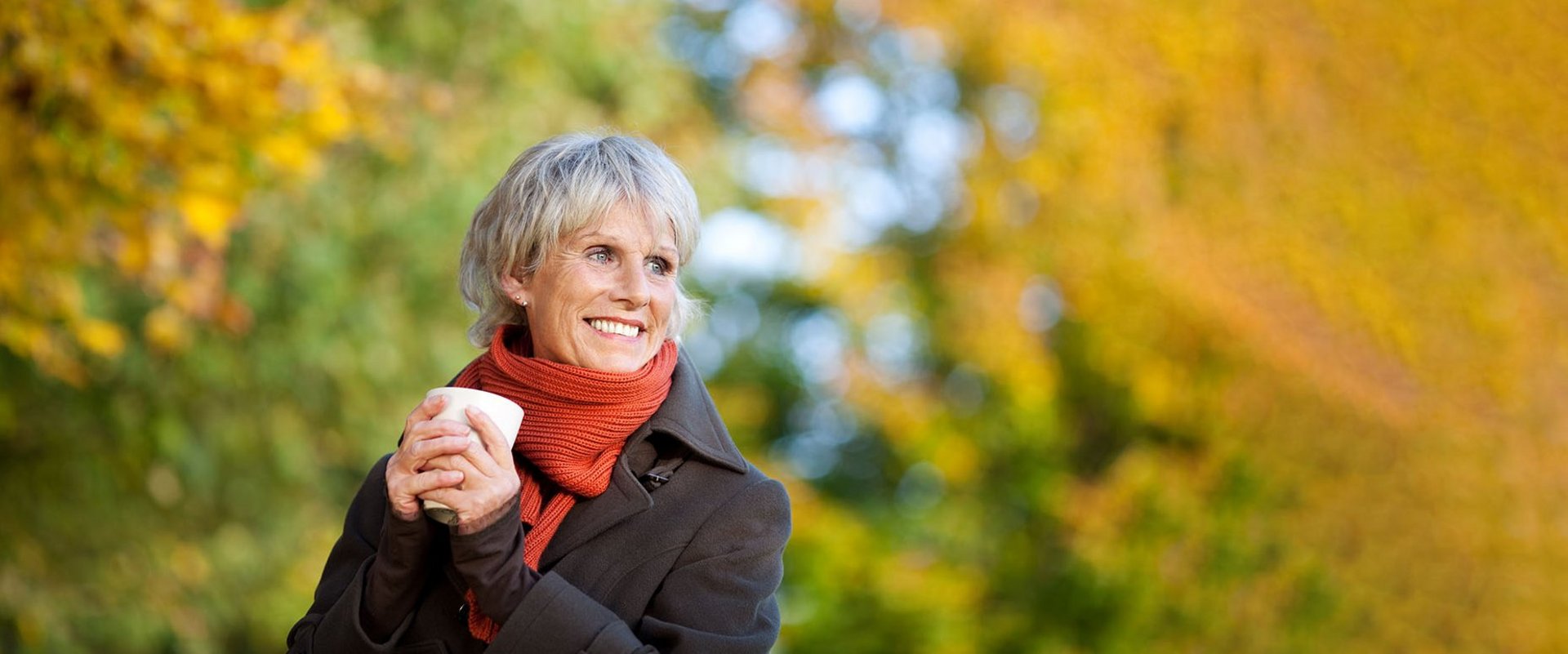 Eine Frau hält eine Tasse in der Hand und genießt draussen den Herbst