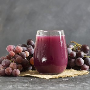 Ein Glas Saft mit Weintrauben im Hintergrund.