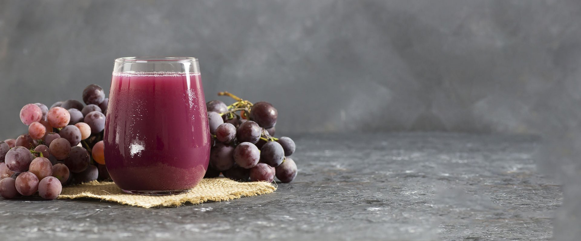 Ein Glas Saft mit Weintrauben im Hintergrund.