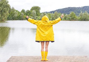 Eine Frau steht an einem See mit einem gelben Regenmantel im Regen